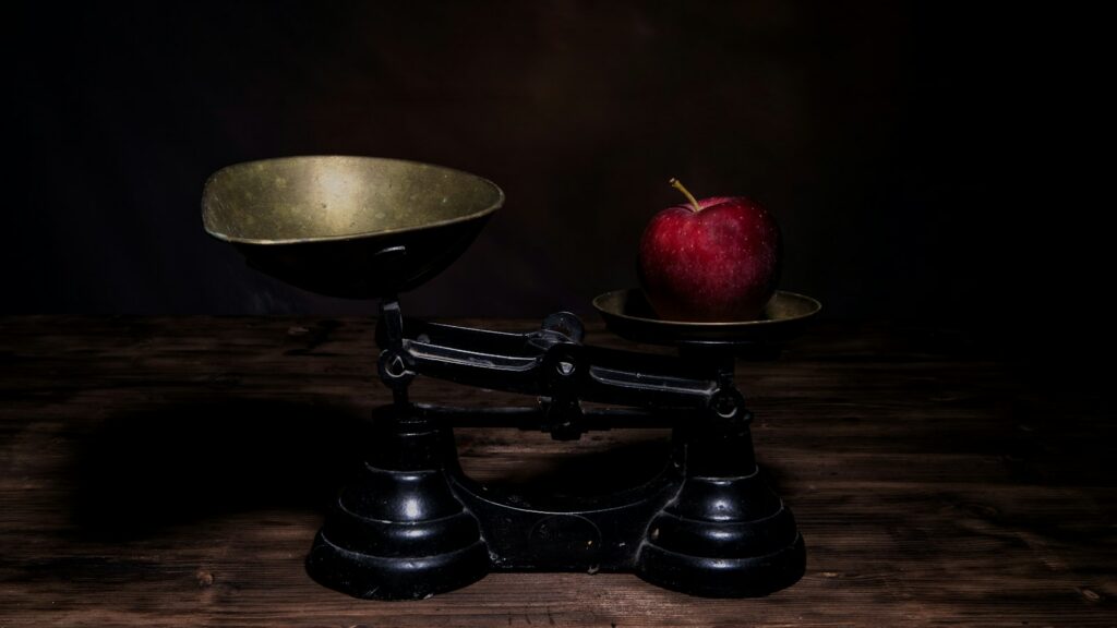 A single apple on one pan of a balance scale outweighing the empty pan
