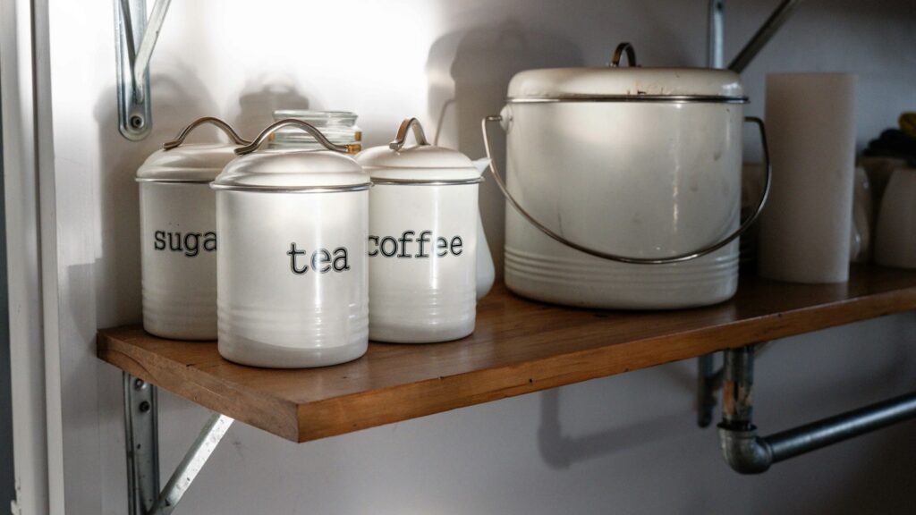 Three canisters on a wooden shelf labelled sugar, tea and coffee