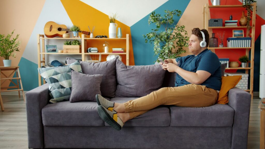 A person relaxing on a couch at home with headphones and a phone
